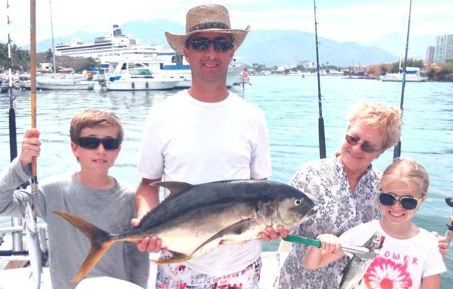Family holding a roosterfish on a Puerto Vallarta fishing charter with the city and cruise port behind
